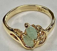 Close up front angled view of ring showing two marquise-shaped light blue jade gemstones on gold electroplated band and inside stamp mark.