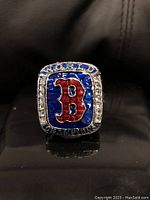 Front view of ring with blue enamel face and red 'B' surrounded by stones and 'WORLD' inscription