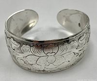 Front angled view showing detailed floral engraved pattern on the silver-toned adjustable bangle cuff bracelet.
