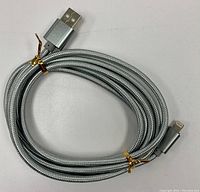 Photo of coiled grey braided charging cord showing USB Type-A and Lightning connectors secured with gold twist ties.