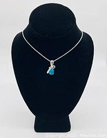 Blue gemstone pendant on sterling silver necklace displayed on black mannequin bust against white background