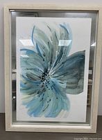 Front view of the framed original watercolor flower painting showing the full artwork with light wood frame and glass reflecting surroundings.