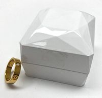 Full view of the gold-tone band ring placed next to a white geometric ring box, showing overall style and presentation.