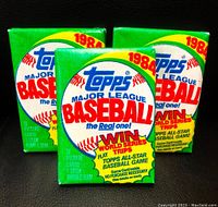 Photo showing three unopened packages of 1984 Topps Major League Baseball trading cards, green packs with red and blue text and promotional offers.