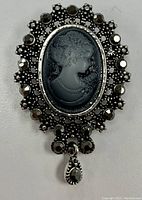 Close-up front view of the vintage rhinestone cameo pin brooch showing the detailed black cameo profile and rhinestone frame with dangling teardrop accent.