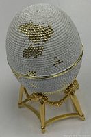 Side view of white textured egg with gold patches on a gold-tone stand