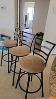 Set of three metal bar stools with beige cloth covered swivel seats and black metal frames