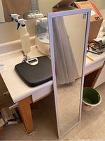 Photo showing black Health-o-Meter digital body scale with digital display on bathroom counter with scissors on top and white cylindrical humidifier next to it, and a large white framed wall mirror standing against wall.