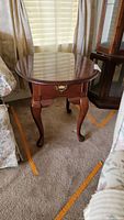 Front angle view of Broyhill wood grain end table with curved legs and drawer, shows shape and style