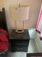 Photo of black end table with marble top and oval-shaped decorative lamp on top, showing overall condition and style.