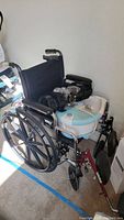 Black manual wheelchair with foot bath/massager placed on seat and a knee brace draped over the armrest.