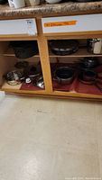 Bottom cupboard showing various pots, pans, roaster pan and Rival ice cooker stored inside.