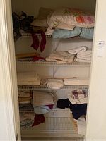 Closet shelves with assorted folded linens including pillows, towels, sheets, and blankets.