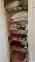 Photo of closet shelf with folded large pillows on top, assorted blankets, folded towels, and stacked linens visible