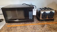 Wide shot of a black Rival microwave and a stainless steel 4-slice toaster on a kitchen counter.