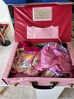 Open pink vinyl carrying case containing assorted doll clothing