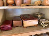Five items displayed on a wooden shelf: three wood boxes and two metal and glass containers.