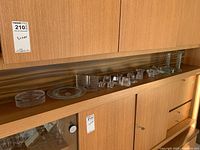 Wide view of all glass candle holders and ashtray pieces arranged on wooden shelf.