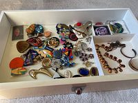 Full view of the jewelry lot showing assorted brooches, pins, wristbands, and necklace in a white tray