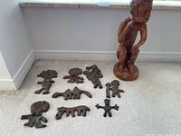 Overview photo showing a group of nine bronze figurines arranged on carpet and a large carved wooden child sculpture seated on the floor.