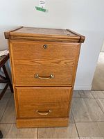 Front view of the wood filing cabinet showing two drawers with brass handles and a lock on the top drawer.