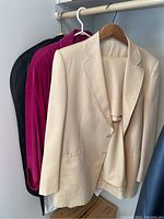 Three jackets hung on a rack: a white/light beige jacket, a bright pink jacket (Danier suede), and a black jacket (Harrington), highlighting the color and styles.