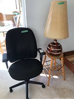 Photo showing black office chair, wood stool, and mid century table lamp with pleated shade and ceramic base.