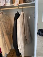 Two jackets hanging in a closet, one black and one white.