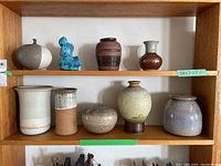 Full shelf photo showing all nine pottery pieces together in two rows, varied shapes and finishes