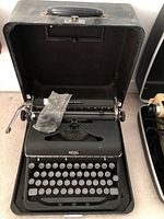 Front view of Royal Quiet De Luxe manual typewriter in open black carrying case, with plastic bag on the machine.
