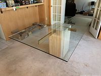 Angled front view of the entire dining table showing glass top, brass supports, and travertine base