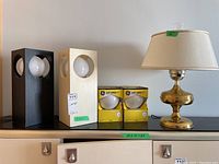 Photo showing the two rectangular table lamps, two boxes of extra bulbs, and the brass hurricane lamp with shade on black surface.