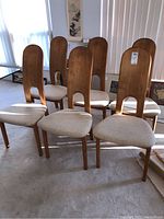 Group of six teak dining chairs arranged in room under natural light