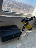 Yellow telescope and mini tripod positioned next to closed black metal case on floor