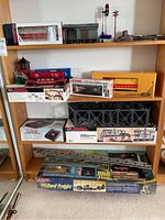 Multiple Lionel train items arranged on wooden shelves showing loco, caboose, accessories, bridge, trestle set and transformer