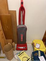 Full view of Oreck Commercial XL upright vacuum cleaner standing against a wall with some replacement bags and manuals at its base.
