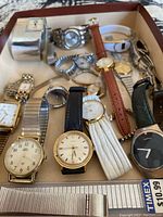 Photo showing assortment of men's and women's watches in box including Timex, Fossil, and various other brands with metal and leather bands.
