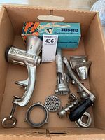 Box with Alexanderwerk meat grinder and various metal accessories including grinding plates, hand crank, clamp, tubing attachments, and Jufru fruit press in box.