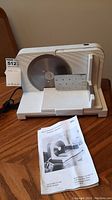 Front view of Braun food slicer showing circular blade, adjustable food carriage, and instruction manual in front.