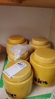 Four yellow speckled ceramic kitchen canisters labeled coffee, tea, flour, and cookies, arranged on a shelf.