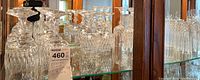 Shelf of multiple crystal wine glasses and goblets with ornate stems reflecting light