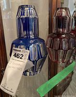 Two cut to clear crystal decanters in blue and red with matching glasses inside a display cabinet.