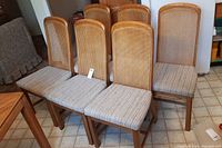 Front and side view of the six rattan and wood dining chairs with upholstered seats arranged in a kitchen area.