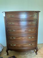 Front view of wooden dresser with five drawers and brass handles, showing scratches and scuffs.