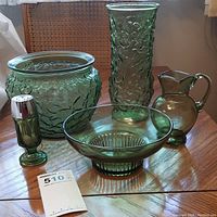 Green textured glass vase, bowl, serving bowl, cream pitcher, and spice shakers displayed on wooden table, showing varying textures and patterns.