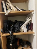 Shoe shelf with multiple handbags in black, white, and brown colors stacked on wooden shelves, showing variety of handbag styles.