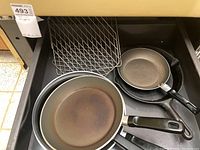 Drawer holding a T-Fal nonstick frying pan, a cast iron skillet, and a wire cooling rack