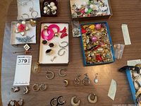 Overview of sterling necklace, bangle and multiple trays of assorted costume earrings laid out on table