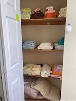 Closet shelf with folded towels and bed linens organized by color across three shelves