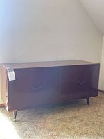 Front and angled side view of veneer record cabinet showing exterior with two doors and tapered legs.
